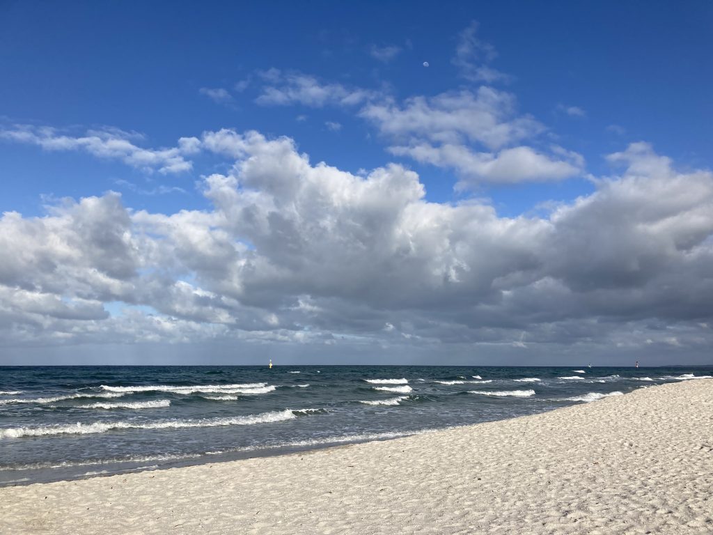 White sand, white-capped waves and a cloudy sky. Brilliant blue above the clouds.