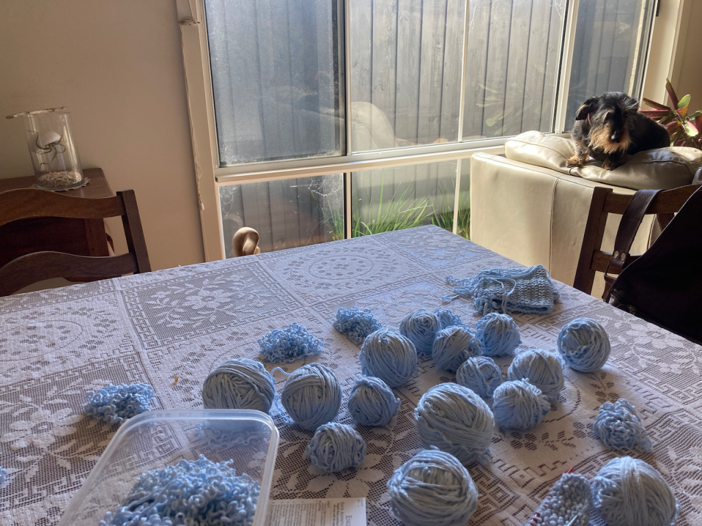 Scout on the back of the couch looking towards a table with balls of bamboo yarn.